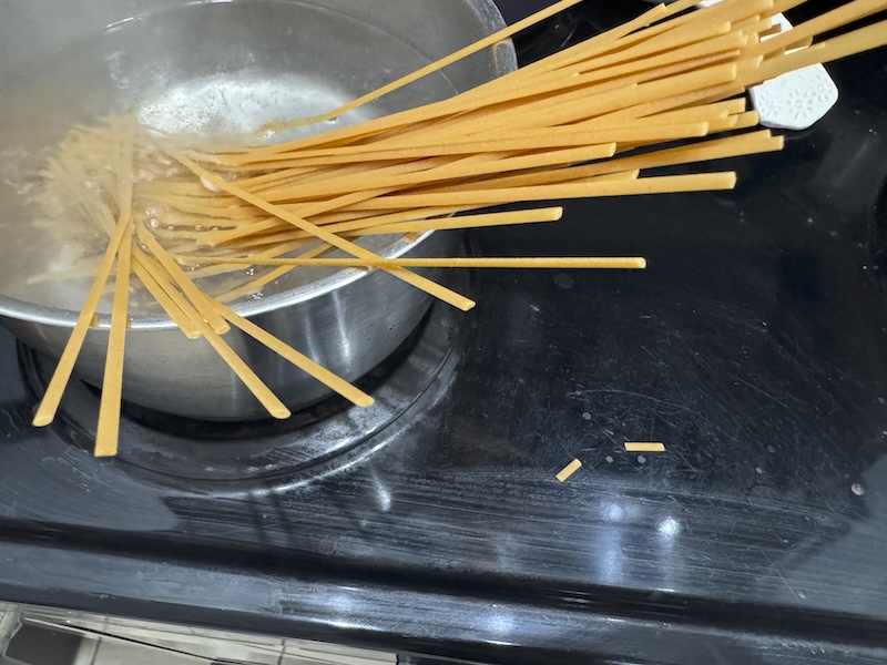 photo of spaghetti just put into a pot. there are some small broken pieces on the stove