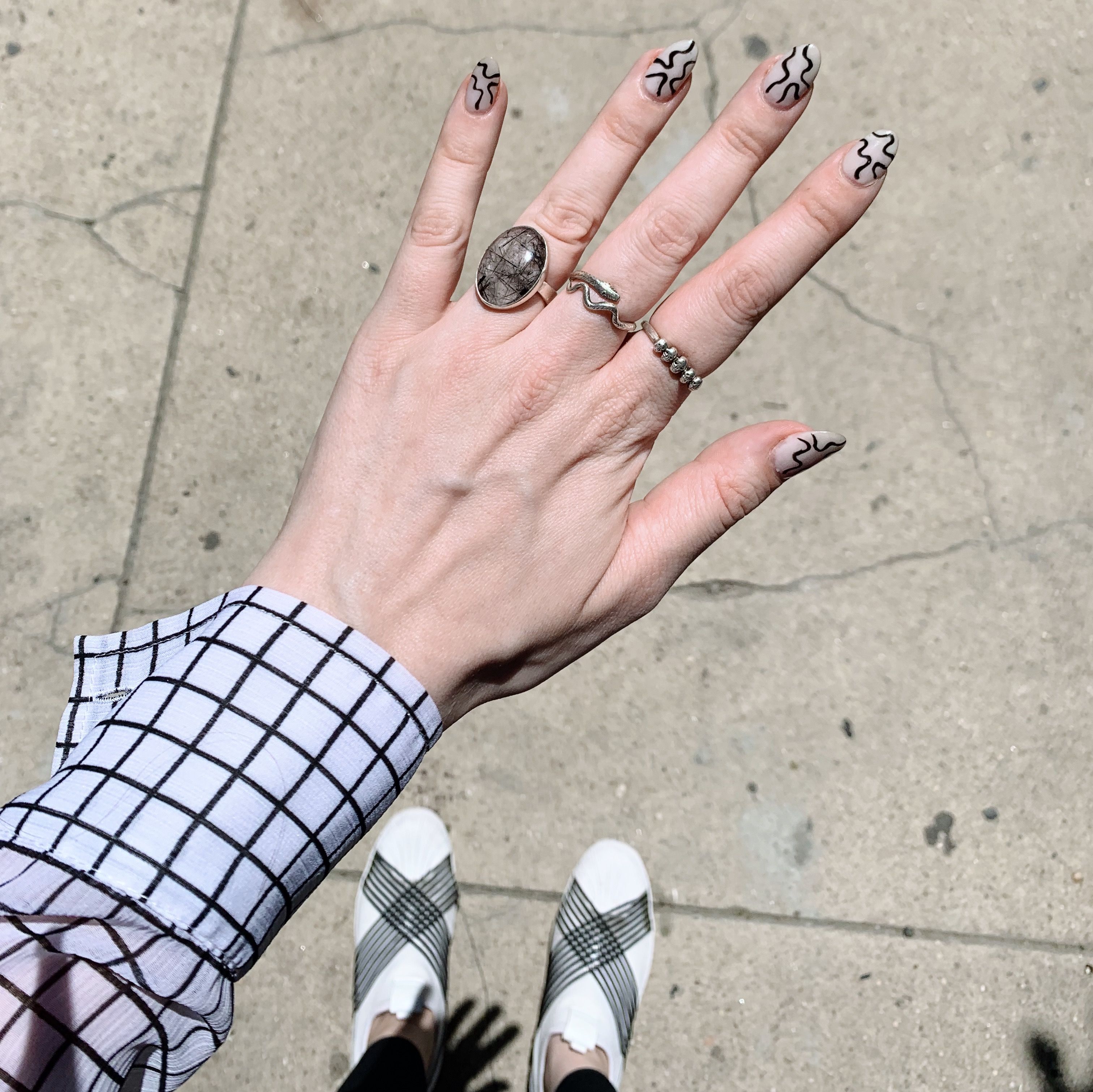 photo of my hand showing a white with black swirl manicure, i'm wearing a white shirt with a black grid all over, and i'm wearing white shoes with thin black stripes on them