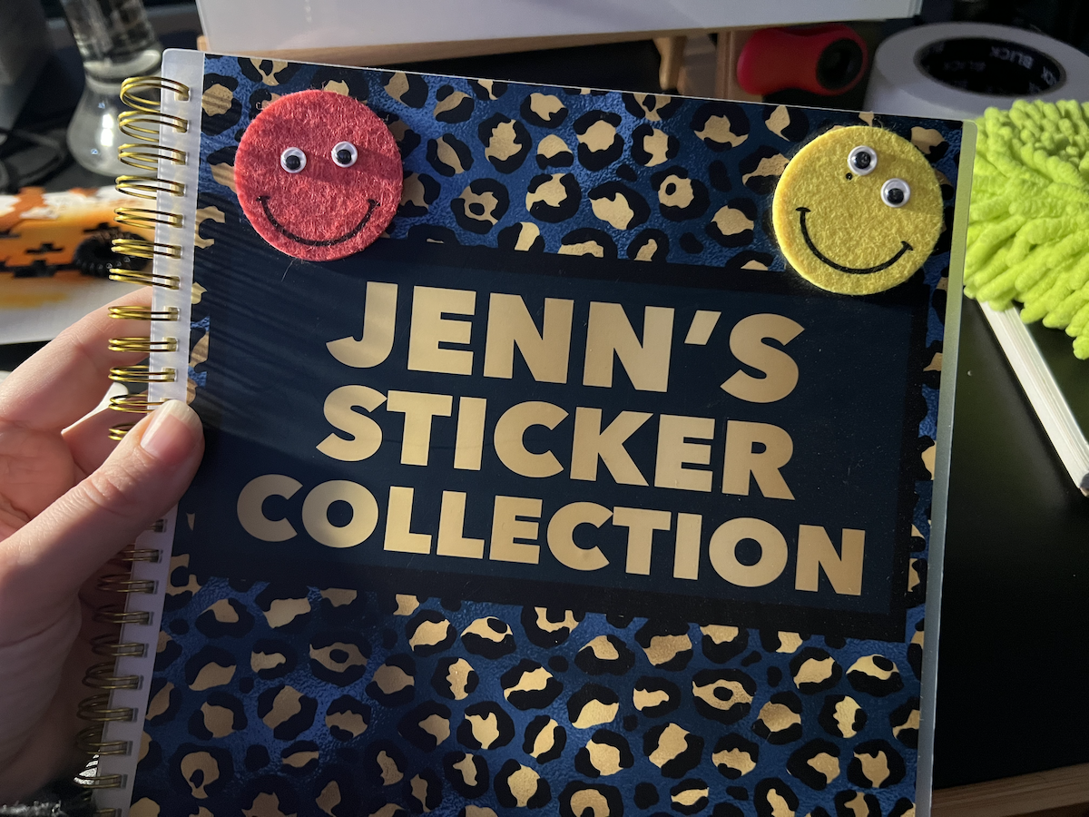 photo of my stickerbook that's 11x7, covered in a blue and gold cheetah print and has big text saying "jenn's sticker book"