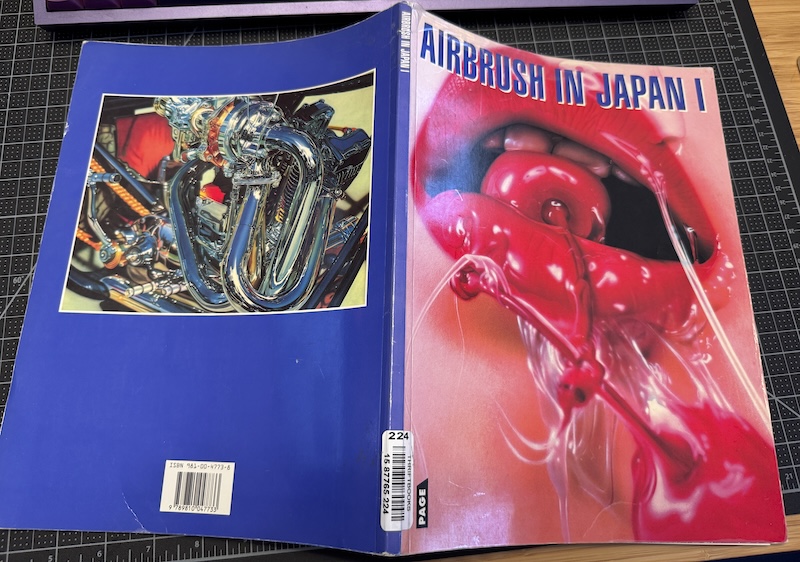 front cover and back covery of "airbrush in japan 1" on my desk, the front c over being an illustration of wet lips softly biting on a maraschino cherry