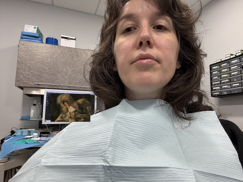 selfie of me in the dentist with my bib on. i replaced the computer screen showing my x-rays with a crop of francisco goya's painting of saturn devouring his son