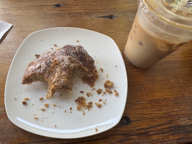 photo of a 2/3-consumed almond croissant next to a 1/3-consumed almond milk iced latte