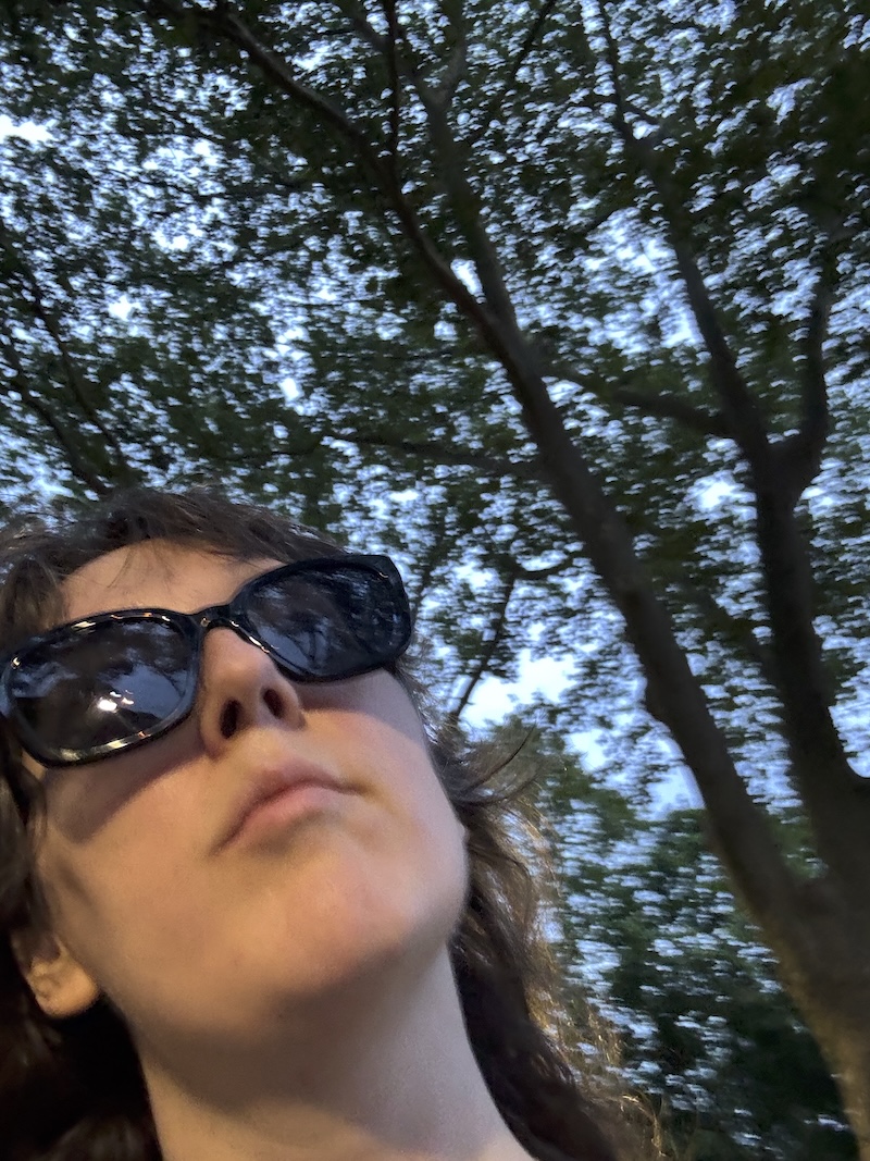 a blurry vertical selfie of me in shades and i'm awkwardly in the left corner and that's because i thought i was photographing in front of me and not in selfie mode