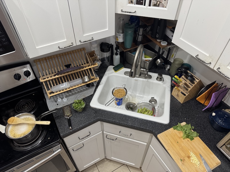 photo of my kitchen that has a corner sink. i'm boiling orzo and i have chickpeas, asparagus, basil and garlic prepped