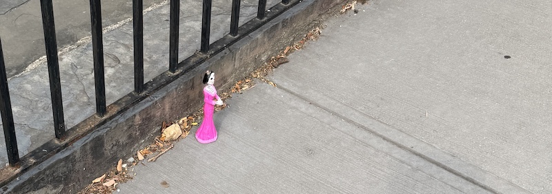 photo of the sidewalk and there's a small skeleton figurine in a pink dress