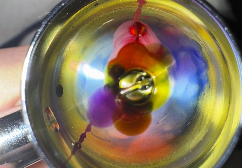 photo of the inside of my airbrush ink cup after a session, there's swirls of liquid watercolor in purple, red, blue, and yellow