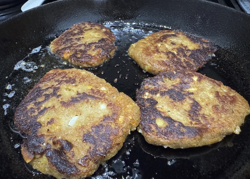 photo of four chickpea cutlets frying in oil inside a cast iron pan