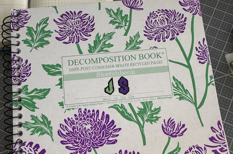 photo of my decomposition book that has purple flowers with green stems and leaves. i wrote "js" with the cool s and a j in a similar style