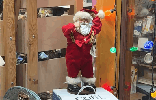 gif of a small santa doll in a store window and it shakes its hips with his hands in the air