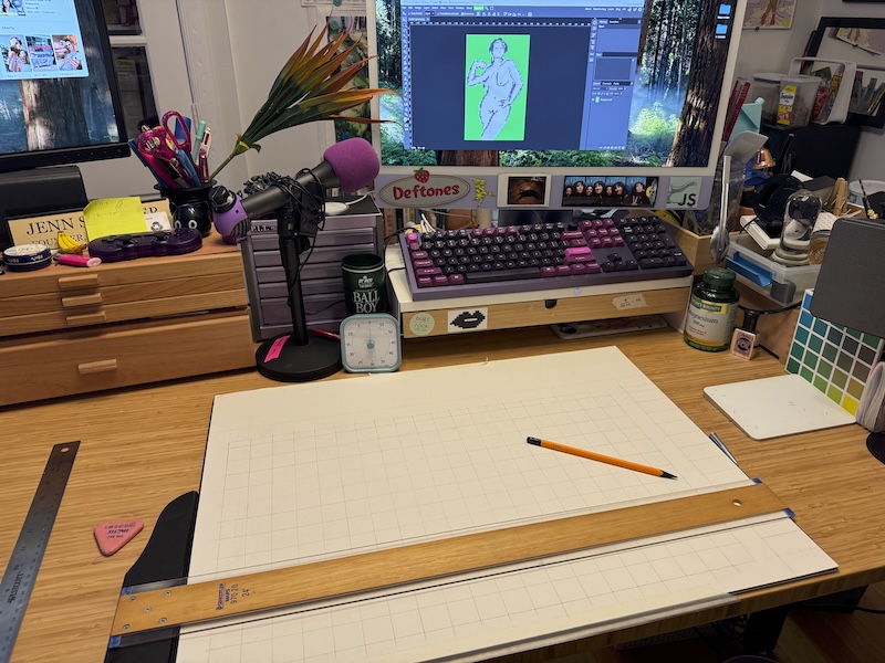 photo of my chaotic desk area and i have a large paper and a tsquare where i'm drawing a grid. on my computer you can see a pixelated figure drawing i made and gave a green background