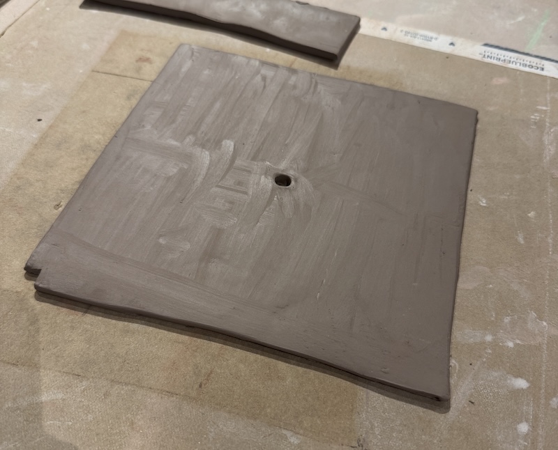 photo of a wet square slab of speckle clay that i've cut a little hole in the middle and will soon be a clock