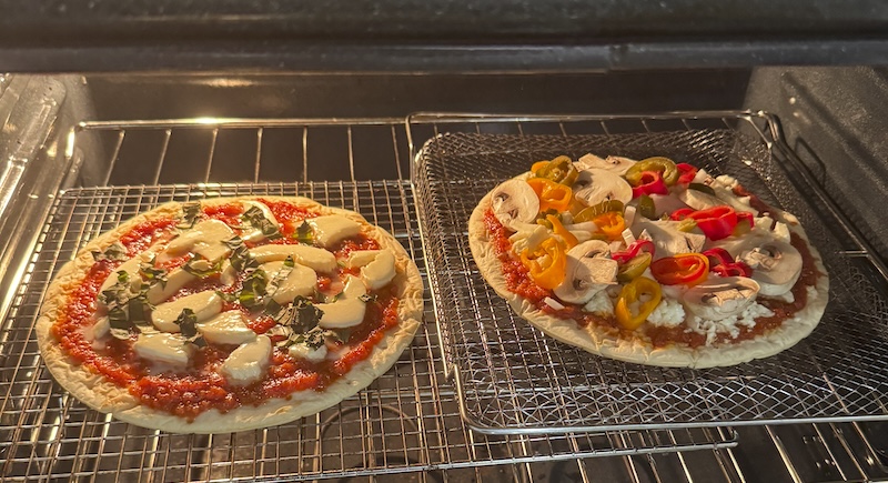 photo of two pizzas in the oven, light on