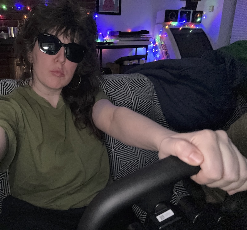 photo of me looking very cool with shades inside our dark living room as i'm behind the steering wheel of andy's gaming rig