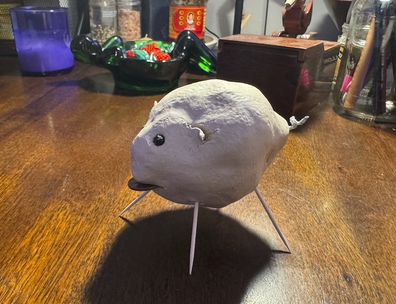 photo of my air-dry clay lemon pig that i put peppercorns in for eyes, a tin foil curly tail, toothpick legs, and a penny sticking out its mouth. it's still drying, so it's not been painted yet