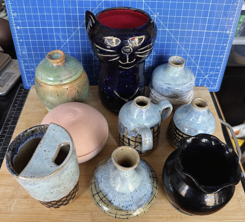 a photo of 9 varied ceramic pieces i made, all together on a wooden cutting board for display. the pieces are described in detail in this post