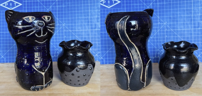 a diptych of a tall cat vase in dark blue with carved details and a black strawberry-shaped smaller vase. the left is the front of them, the right side is the back side which shows the cat has matte legs and a tail added as slab pieces for some more dimension