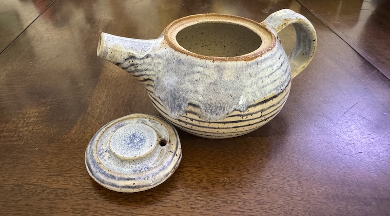 a photo of a white teapot with black horizontal stripes all around and it's like the top half was dipped in a periwinkle glaze that dripped down and melted some of the lines. i have the lid off and to the side.