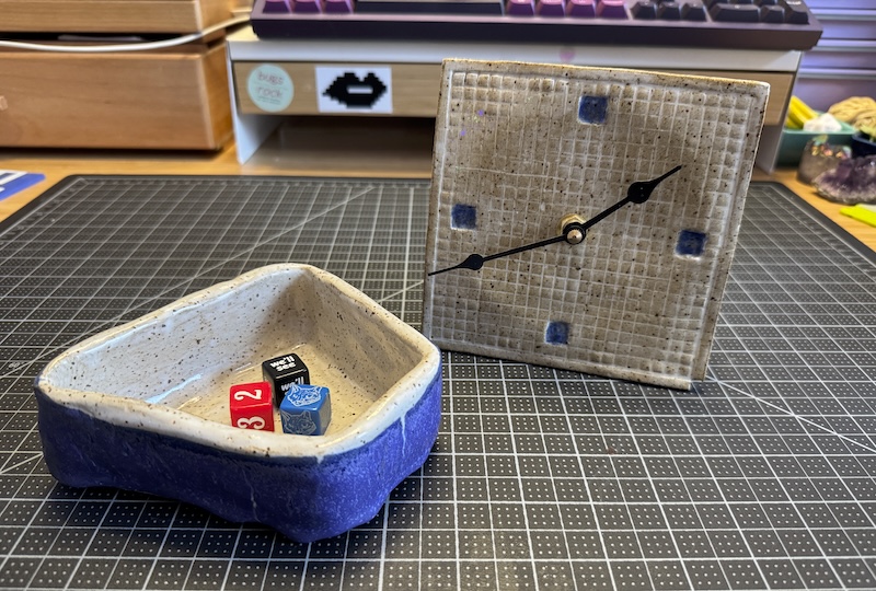 a trapezoid coil pot with a few dice inside to show size, and next to it is my grid paper ceramic clock. i took the photo at 1:40pm it looks like