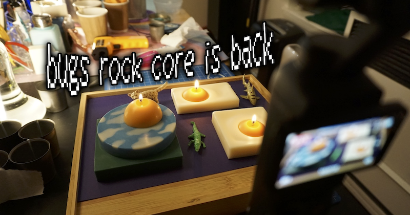 photo of a bugs rock candle wick test being recorded on camera and i added the pixel text "bugs rock core's back"