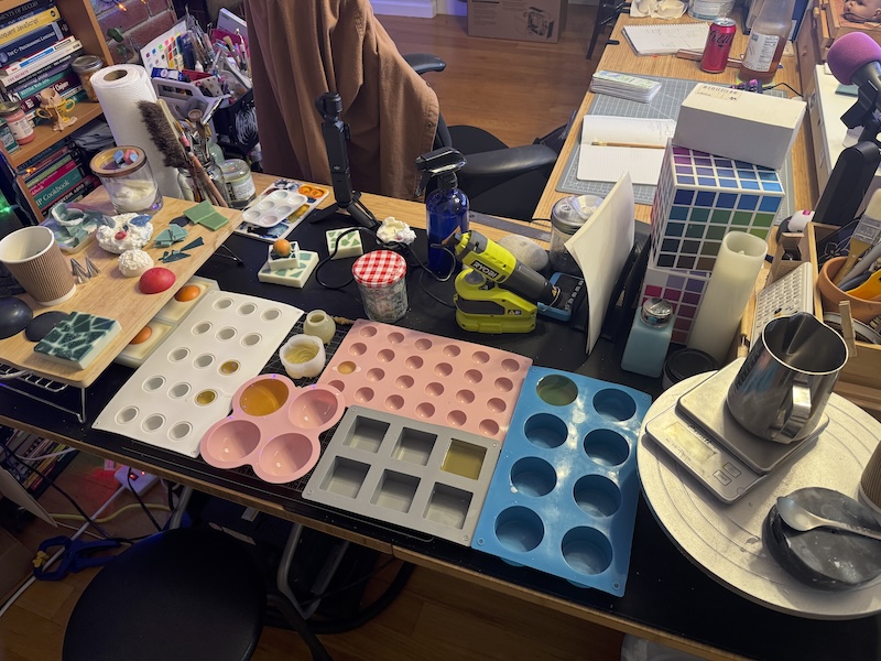 photo of a bunch of silicone molds, some filled with wax, on my L-shaped desk. it looks like a mess but it's actually quite organized