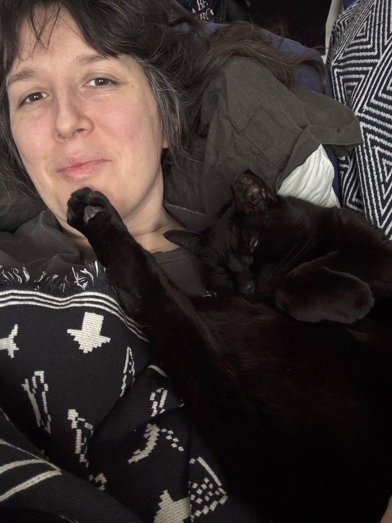 photo of me laying on the couch and my black cat pumagreg is laying on me with his foot straight up into my chin
