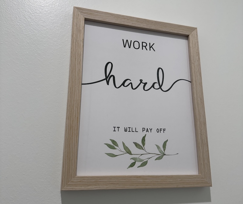 ugly bland gym art framed on the wall that says "work hard it will pay off" in three different fonts