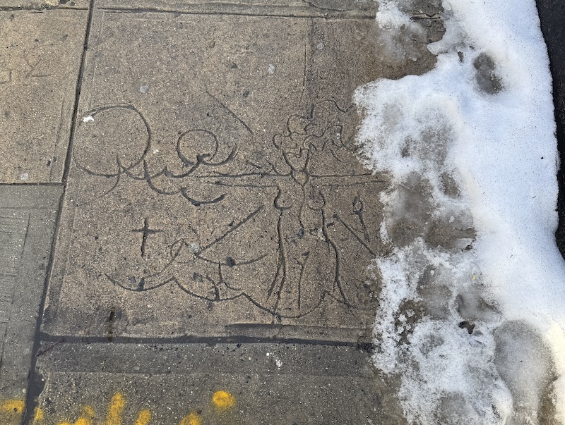photo of a wet sidewalk with snow melting on the side. into the sidewalk when it was wet concrete, someone etched a nude woman with shapes around it. i honestly don't know what it is of and what its meaning is
