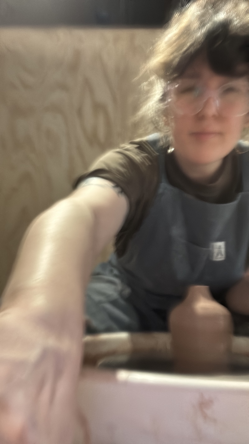 a very blurry selfie of me at the pottery wheel throwing a bud vase