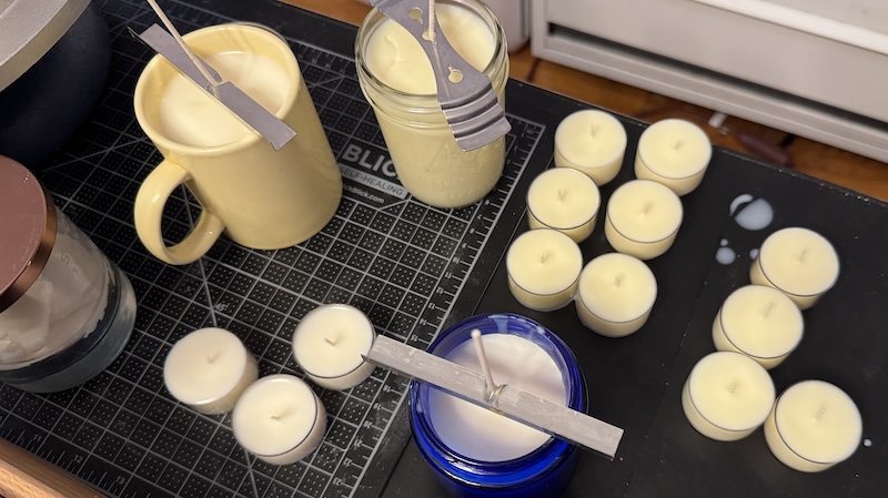 photo of my candle-making zone with a bunch of tealights, a couple of cobalt blue glasses, a mug and a small mason jar all filled with wax and wicked