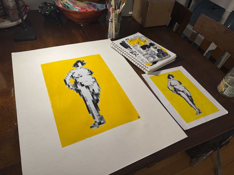 photo of my table after i finished a pixel art figure painting. there's a large paper with the painting - yellow background and grayscale pixel art version of a feminine figure i sketched in real life awhile back. next to the paper is a smaller printer paper where i printed the reference out, and above that is my sketchbook and palette covered in yellow, black and gray paint