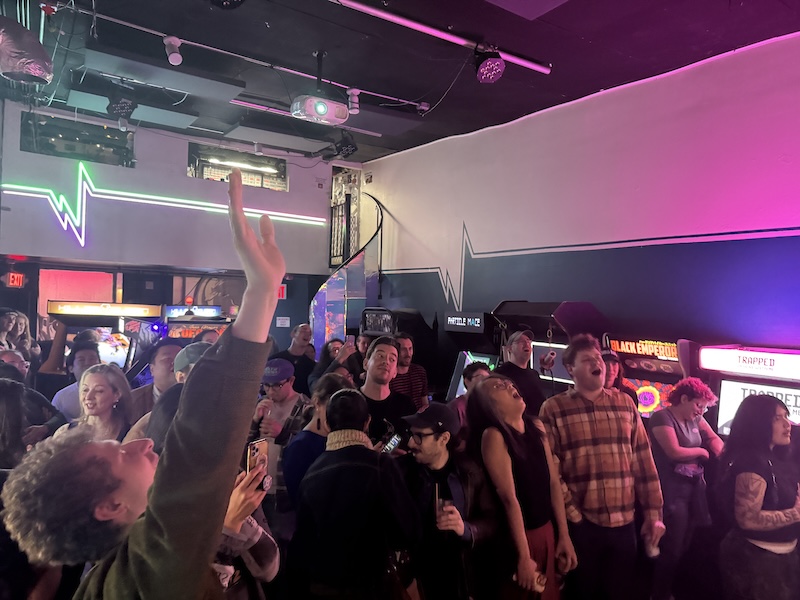 photo of the arcade filled with people singing, arms raised, in the middle of our show