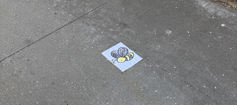 photo of the wet ground with a wet coloring book page of a cartoon bee smiling