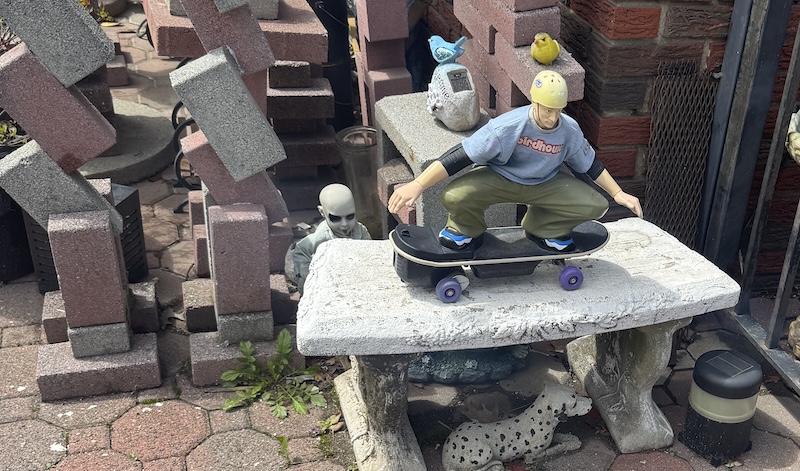 photo of a small tony hawk lawn ornament on a decorative stone bench and surrounded by brick sculpture, a scary baby doll, a dalmation, a rubber ducky