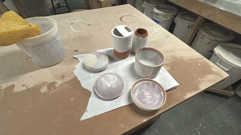 photo of a bunch of just-dipped-in-glaze pots of mine, a couple closed vessels, a travel mug and a cup. they're on the table of the studio near my water bucket and sponge