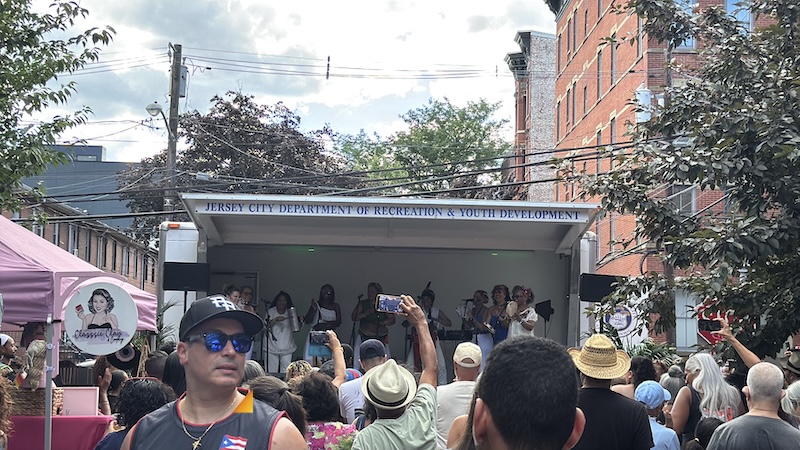 photo of a band playing at a street festival in jersey city with lots of onlookers and vendors on the side