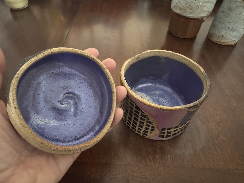 photo of a ceramic cylindrical dish with lid that's purple all around with black grids carved into it. ii'm holding the lid to show the inside is purple