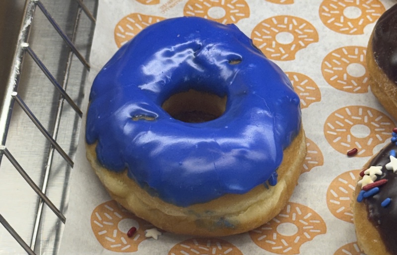 photo of a vanilla donut with primary crayola blue icing on the shelf at dunkin