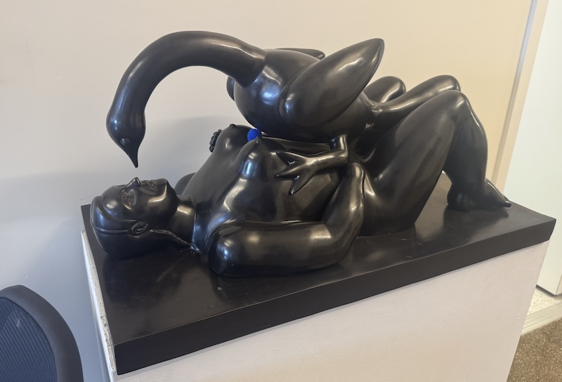 photo of a small version of botero's leda and the swan sculpture in black and there's a little blue pompom between leda's breasts