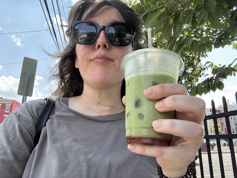photo of me outside holding a strawberry iced matcha latte on a very hot, sunny day post-gym