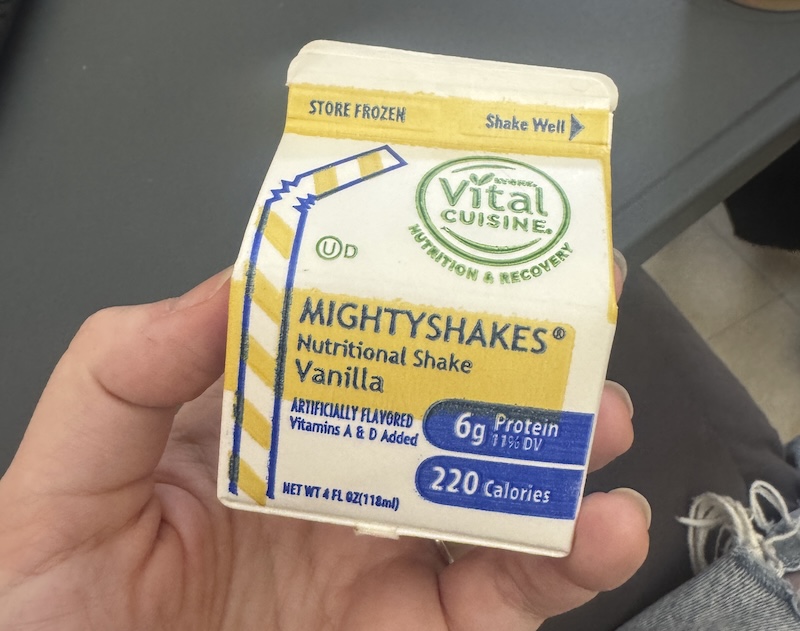 a photo of a small little milk carton of protein shake i'm holding up in my dad's room in assisted living