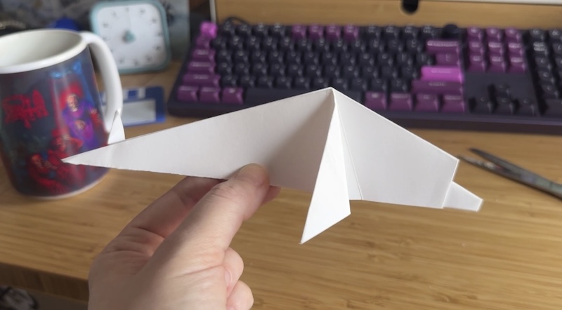 a photo of my hand holding up an origami dolphin i made from white paper