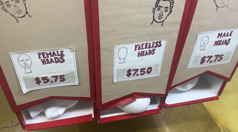a photo of a dispenser at Blick of styrofoam heads that come in, from cheapest to most expensive, "female", "faceless" and "male"