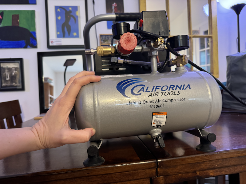 photo of my small air compressor on my table and my hand is on the side of the tank to show its small size