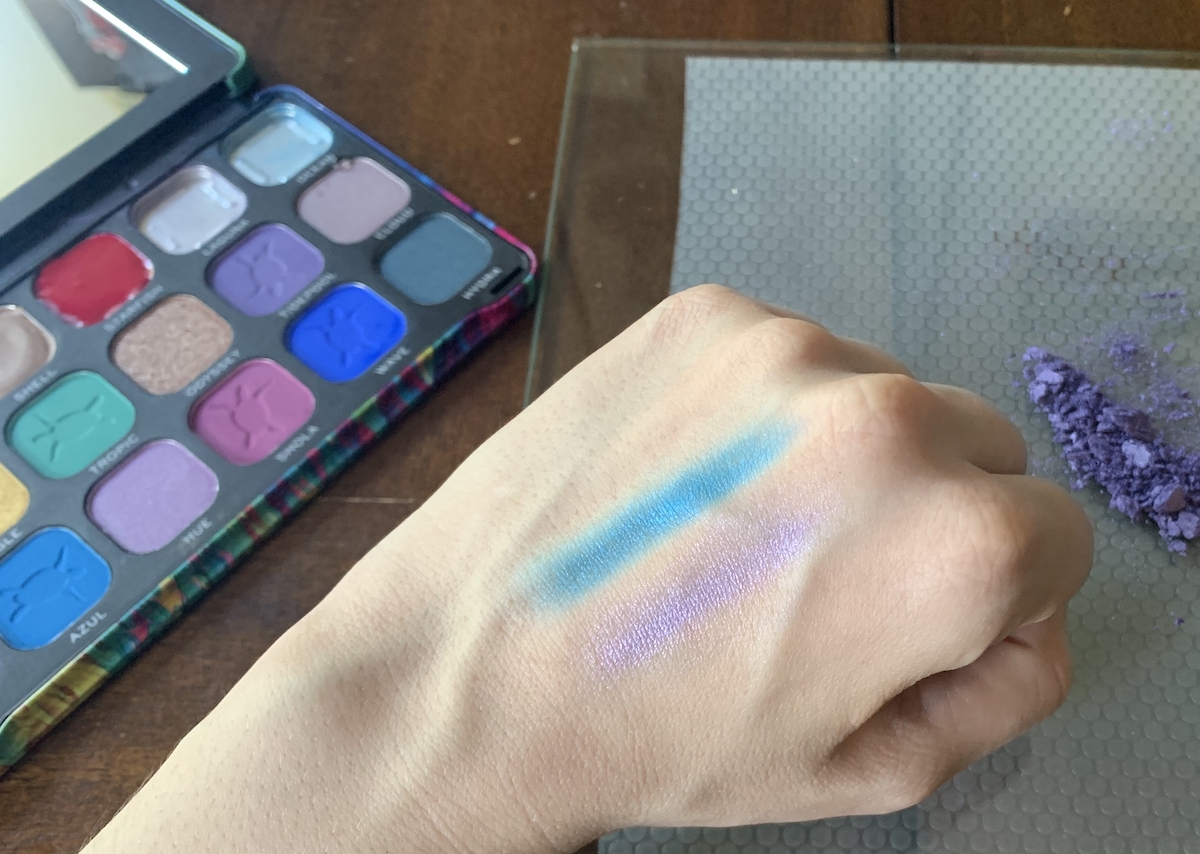 photo of my hand with a blue and purple eyeshadow swatched on it and you can see the palette and my watercolor making gear on the table