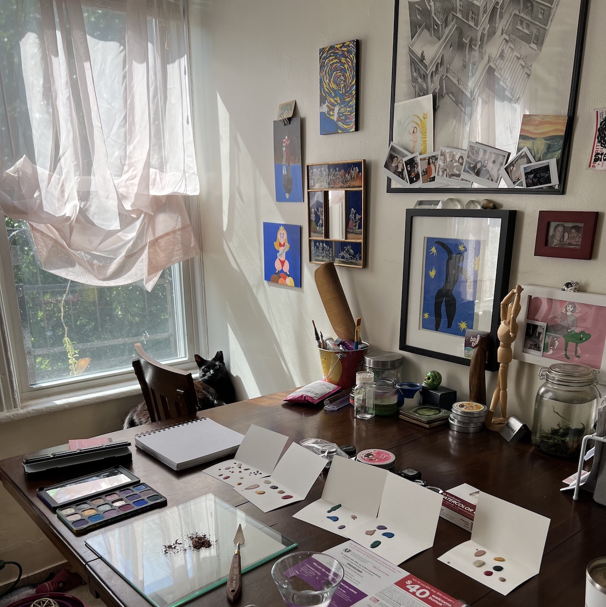 photo of my kitchen table showing my watercolor gear, cards in progress, and my black cat pumagreg creeping in the background by the window