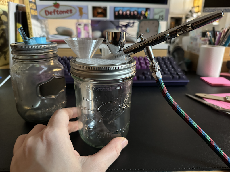 photo of two jars with spray pot 3d-printed attachments. the one in front is wide-mouthed and i have my airbrush inside the attchement so you can see what it's for