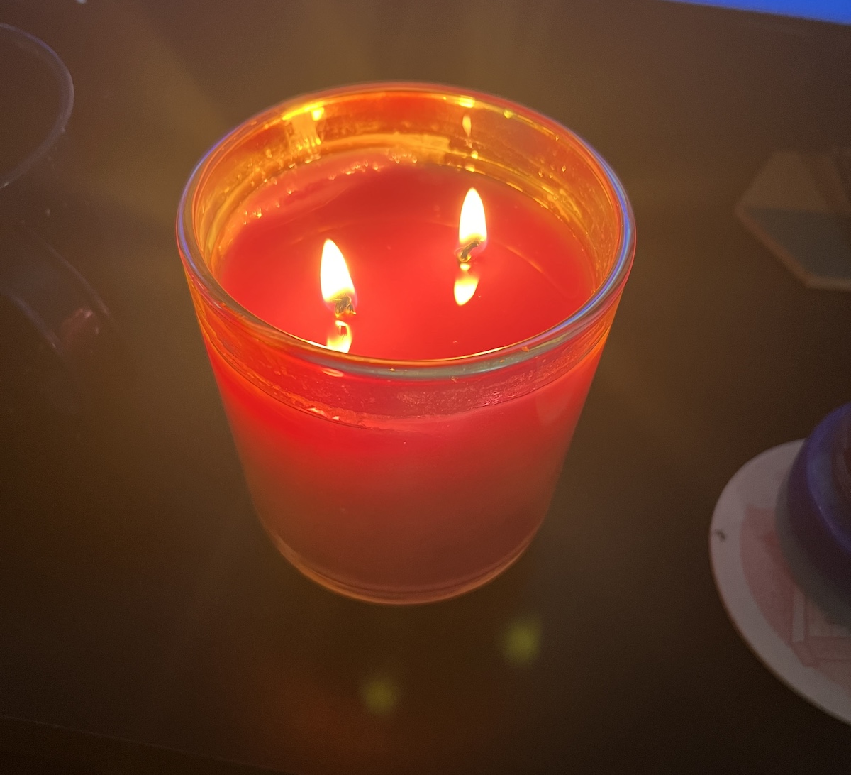 photo of a candle in a glass shot class and 2 small wicks. it's red-orange in color and in front of my old tv