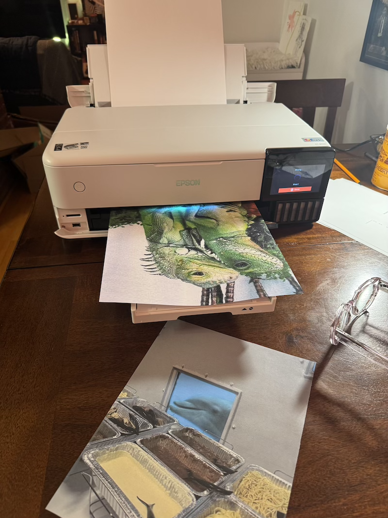 photo of my new printer printing an edgeless poster of two lizards in loving embrace. already printed to the side was an image of a buffet on a submarine and a dolphin is looking through the window at the food