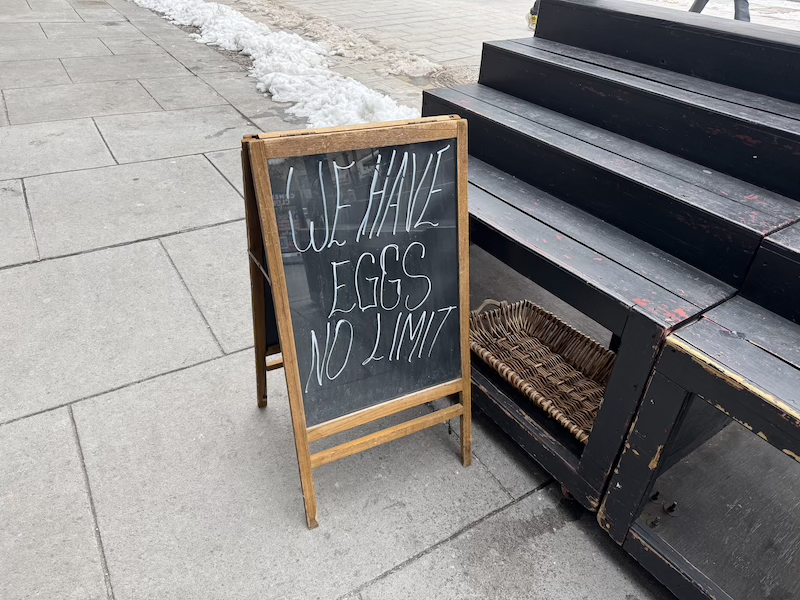 photo of a grocery store chalk sandwich board outside that says "WE HAVE EGGS NO LIMIT"