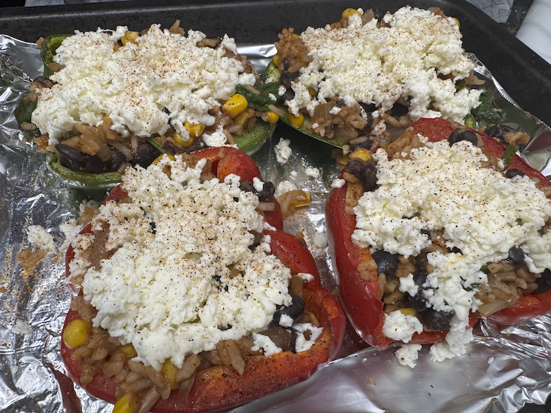 a photo of stuffed bell peppers covered in shredded mozzarella cheese, about to go in the oven